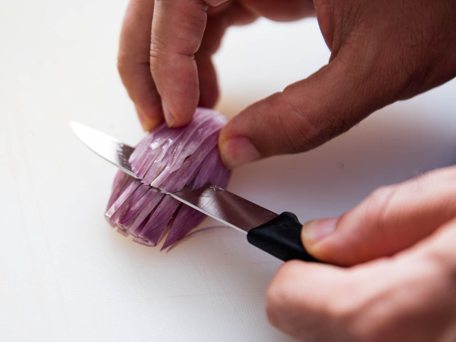a paring knife being used to mince a shallot