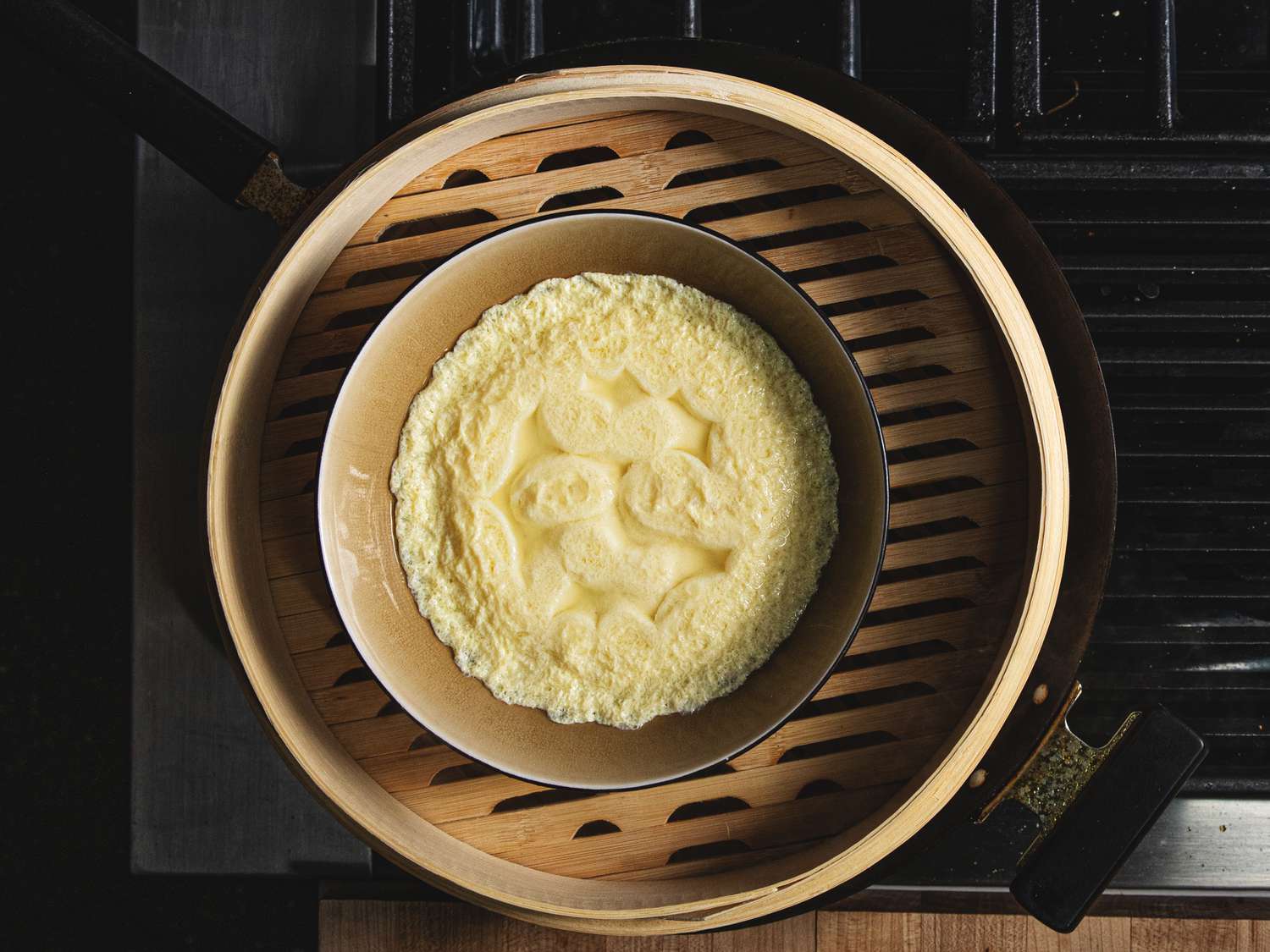 Overhead view of a egg dish steamed in a bamboo steamer on a wok