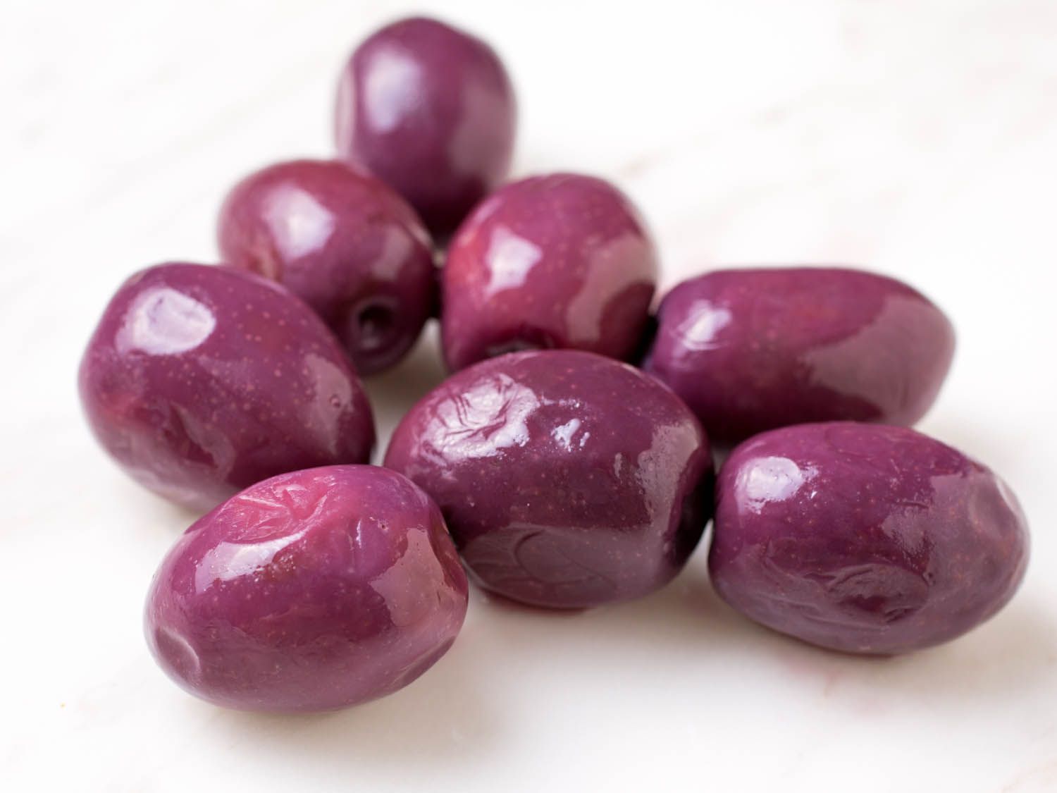 Closeup of slightly shrivelled, bright purple olives on marble surface