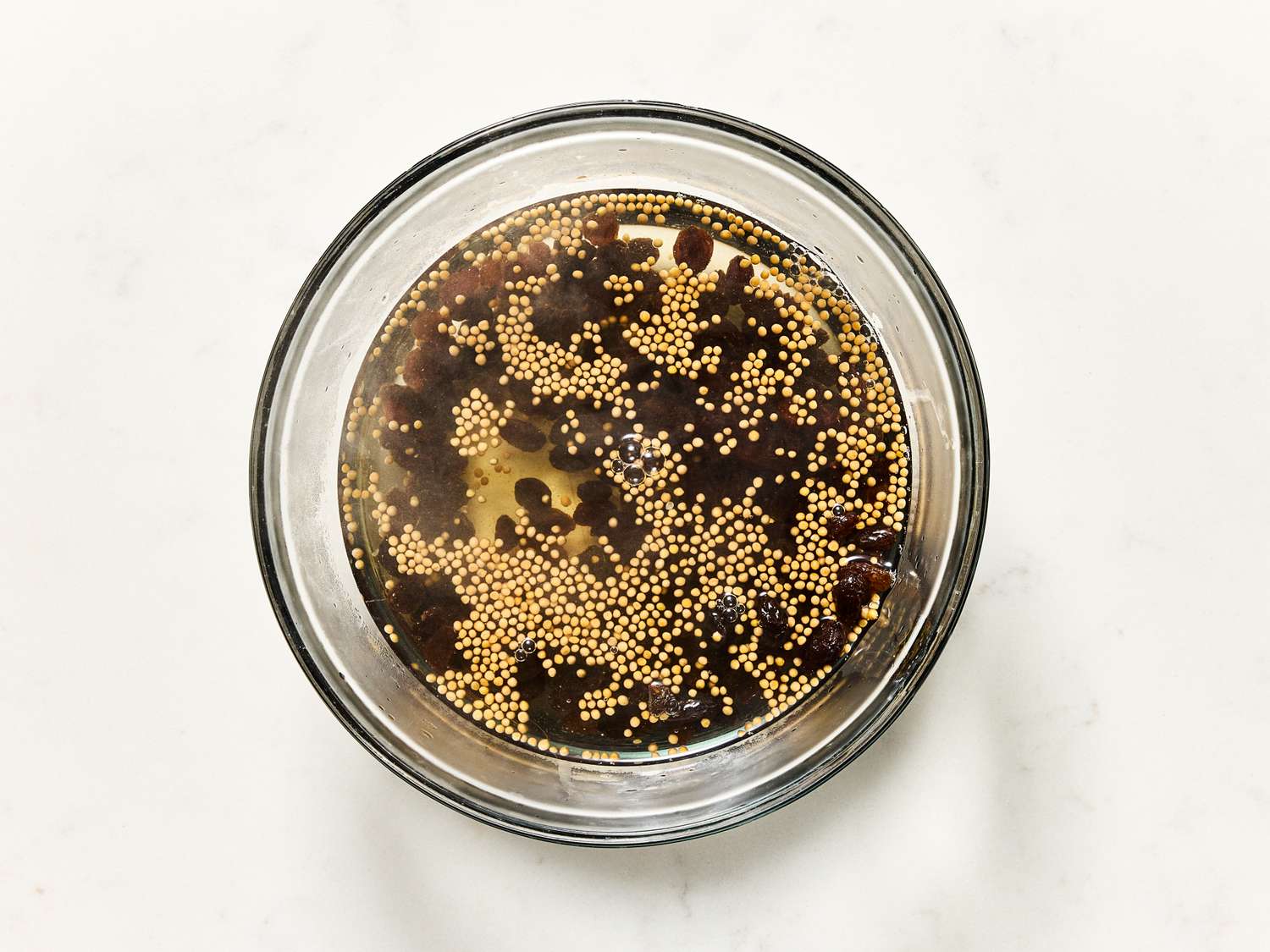Glass bowl containing a mixture of mustard seeds and dark liquid