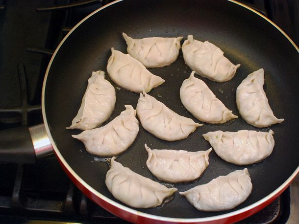 Vegetable dumplings spaced out on a oiled nonstick frying pan.