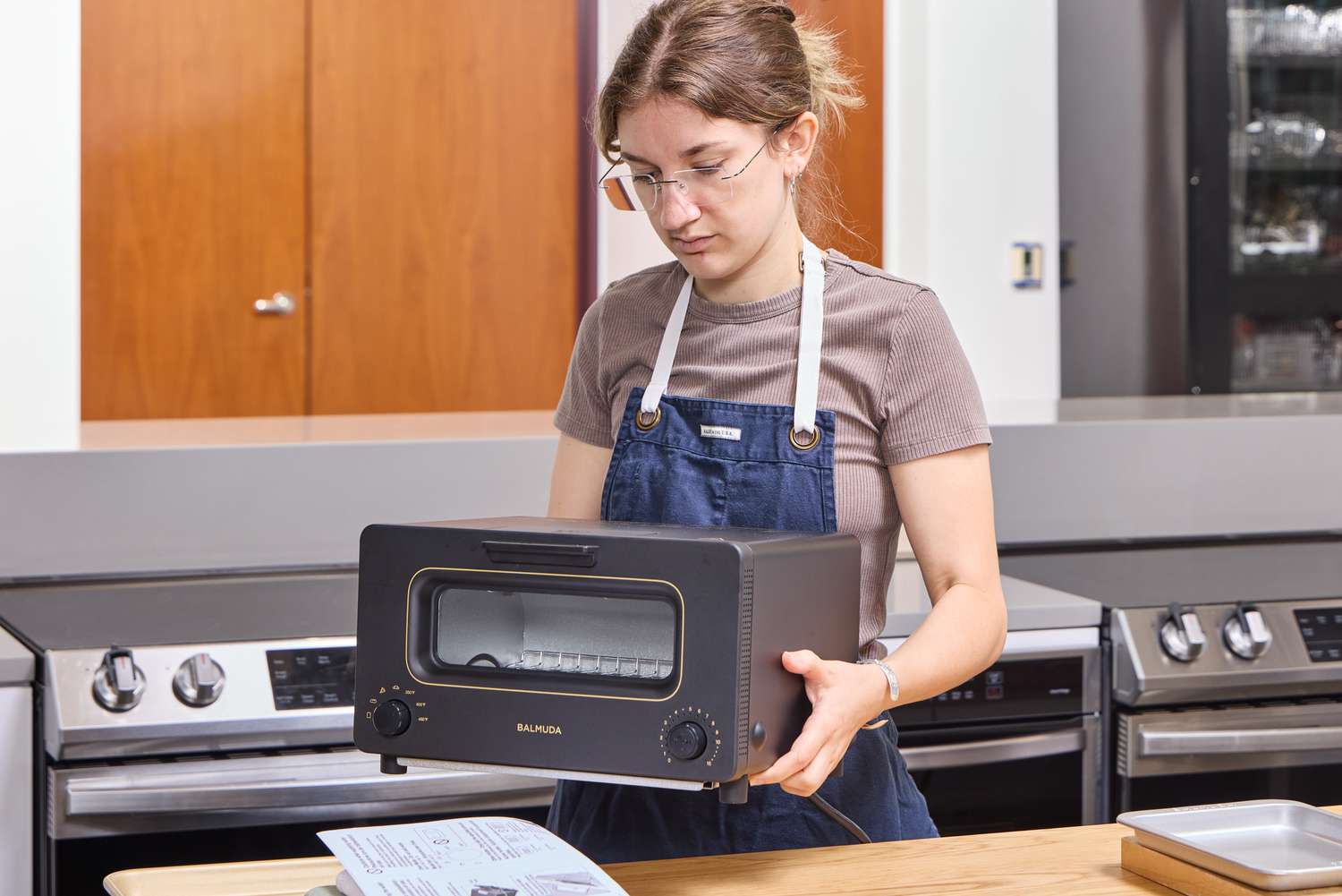 A person holding a BALMUDA toaster in a kitchen environment
