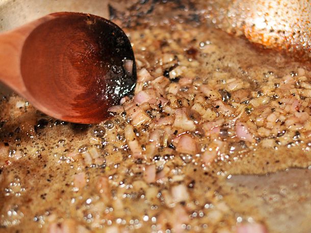 Sautéing shallots in butter in a skillet with a wooden spoon.