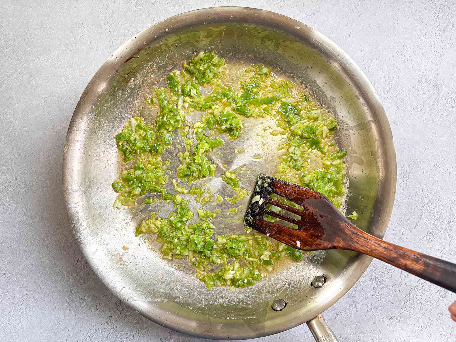 Cooking garlic and green ingredients in a frying pan, with a wooden spatula in use