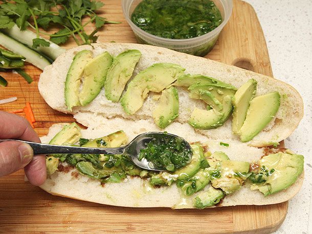 Spooning ginger scallion oil over sliced avocado layered in an opened sandwich roll