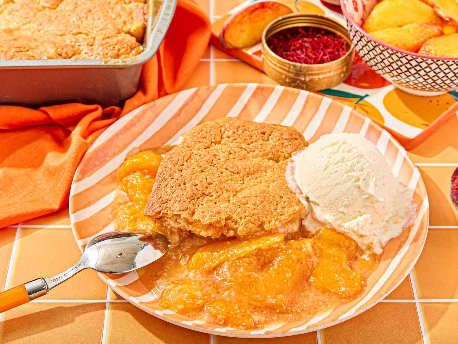 Peach cobbler with a scoop of ice cream on a plate fresh peaches and spices in the background
