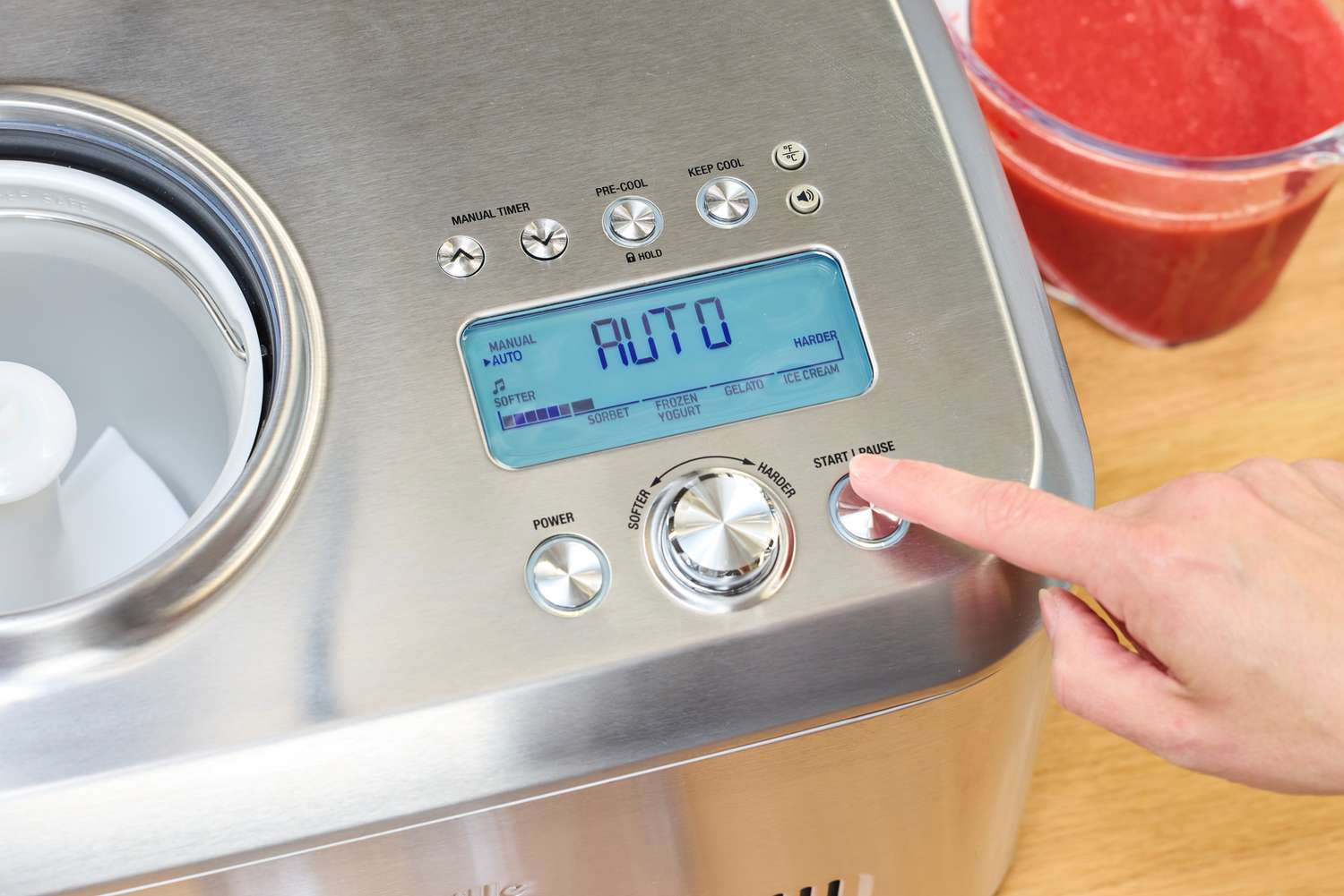 A finger pressing a button on the Breville Smart Scoop Ice Cream Compressor
