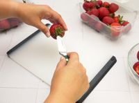 A paring knife coring a strawberry
