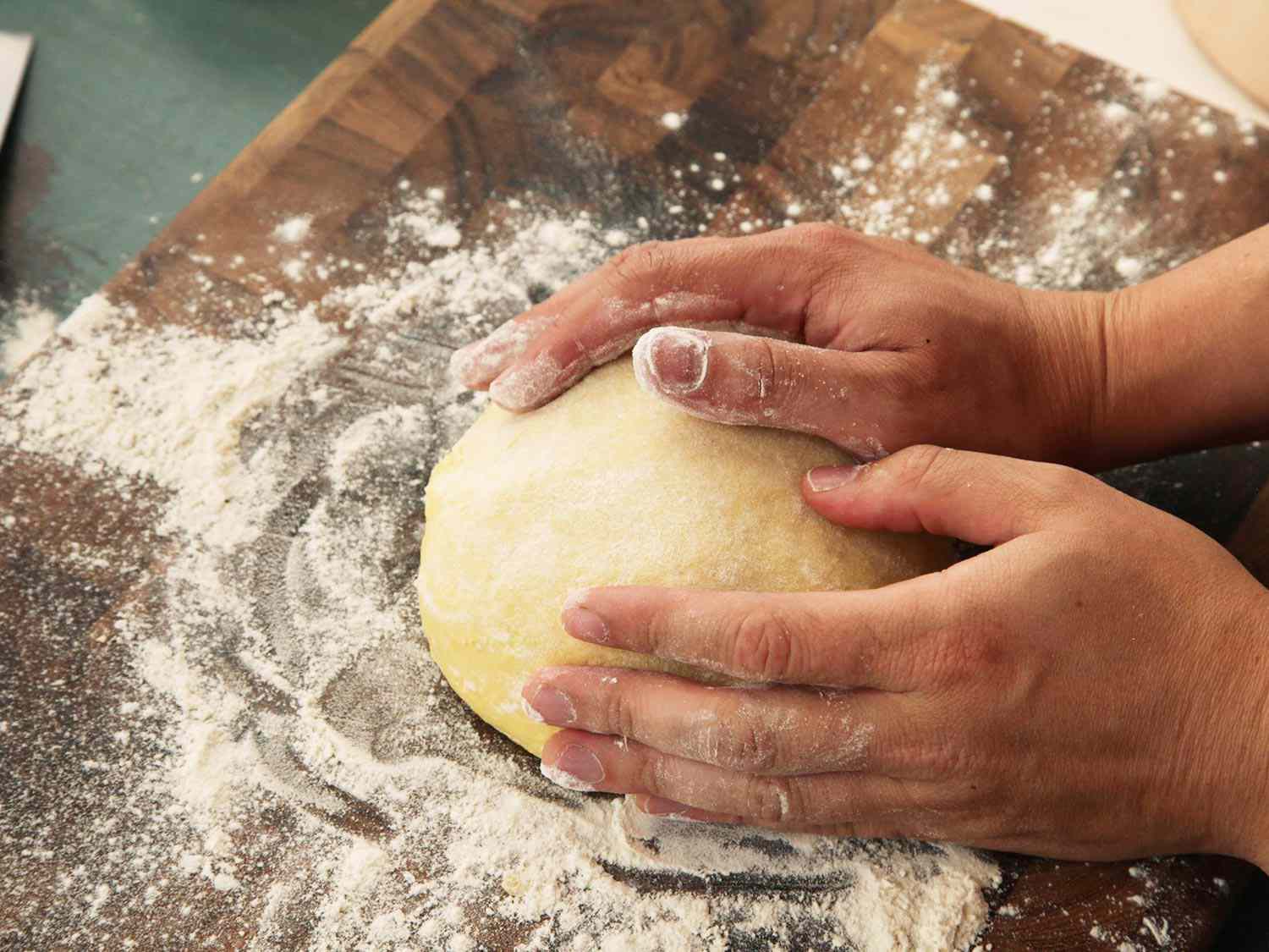 Kneading bread dough with hands on a floured cutting board.