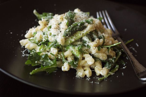 Closeup of gemelli with asparagus, ricotta, arugula, and lemon zest served on a black plate.