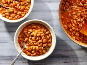 Two bowls and a pot of frijoles charros, on a stone background.