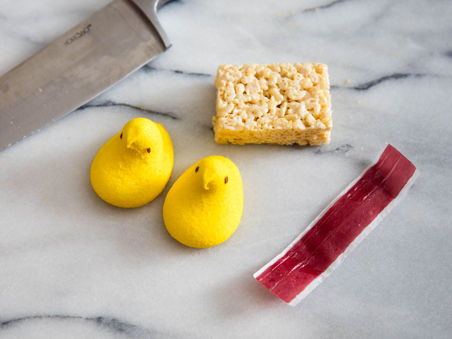 Two yellow peeps, fruit leather, and a Rice Krispy treat on a marble surface with a chef's knife. 