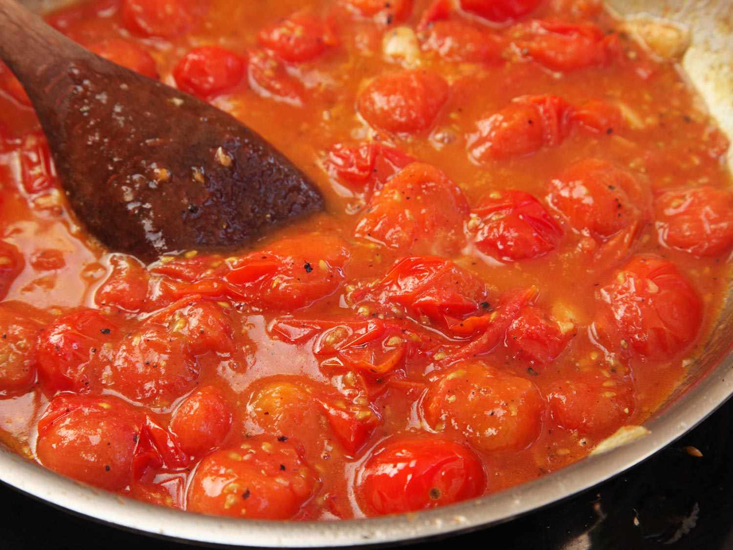 A wooden spoon in a pan of cherry tomato sauce