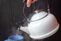 A hand pouring hot water from a kettle into a cup