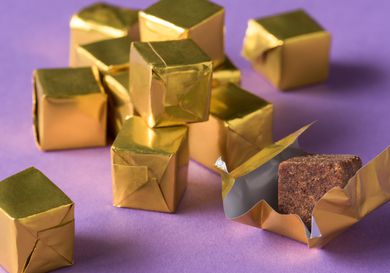 Closeup of a pile of gold foil-wrapped bouillon cubes. One has been unwrapped to reveal the cube itself.