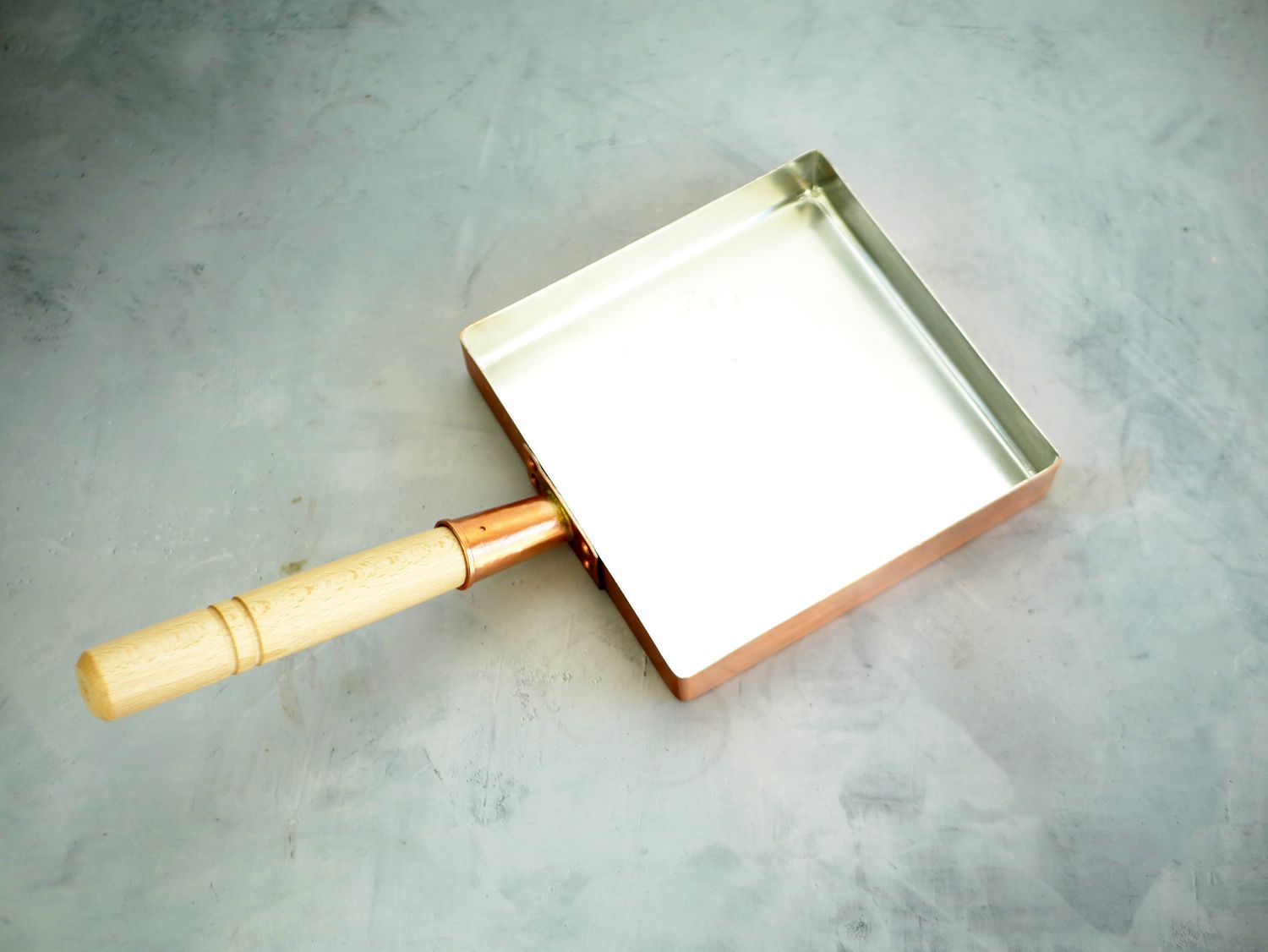 a copper tamagoyaki pan on a gray surface