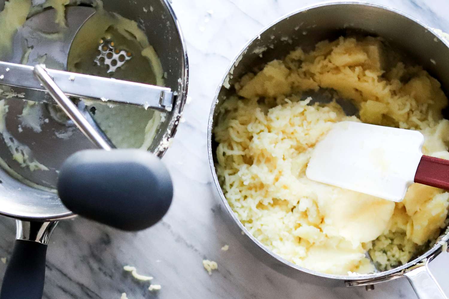 Using a spatula to mix together freshly milled potatoes in a pot with the food mill on the left