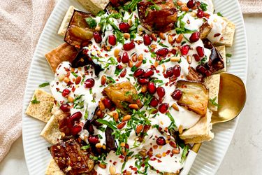 A plated serving of eggplant fatteh garnished with pomegranate seeds parsley and yogurt sauce