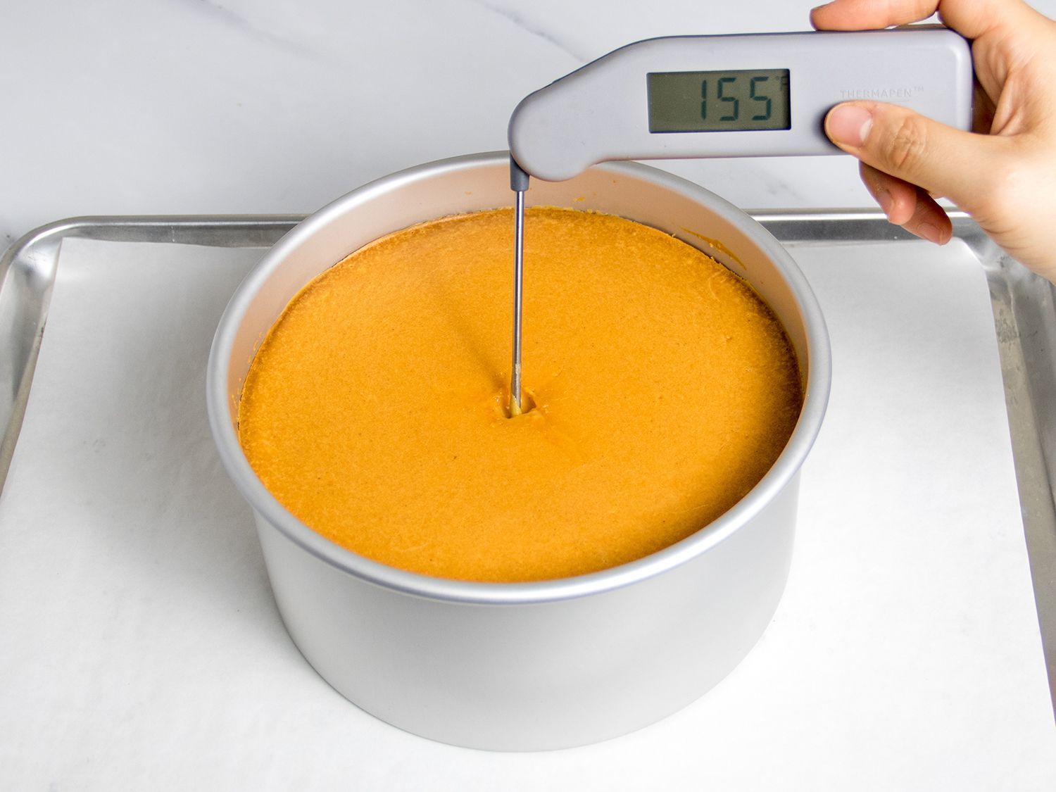 A thermometer inserted in the center of the baked cheesecake shows a temperature of 155F.