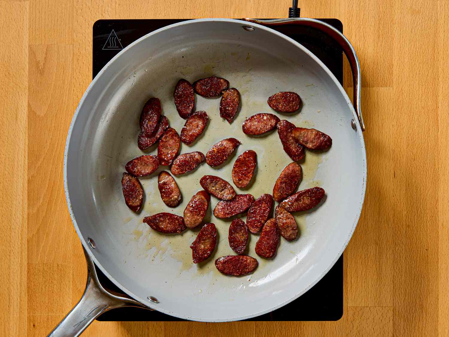 Sliced sausage pieces cooking in a skillet on an electric stovetop