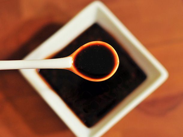 A spoonful of teriyaki sauce being held over a bowl of teriyaki sauce.