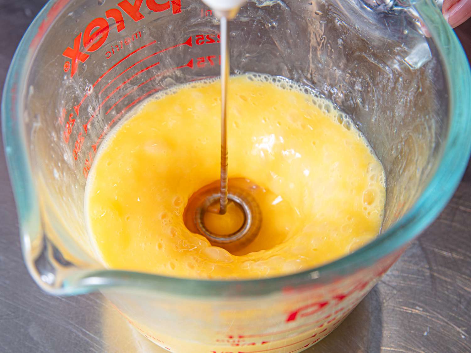 A milk frother blending a yellow liquid inside a measuring cup
