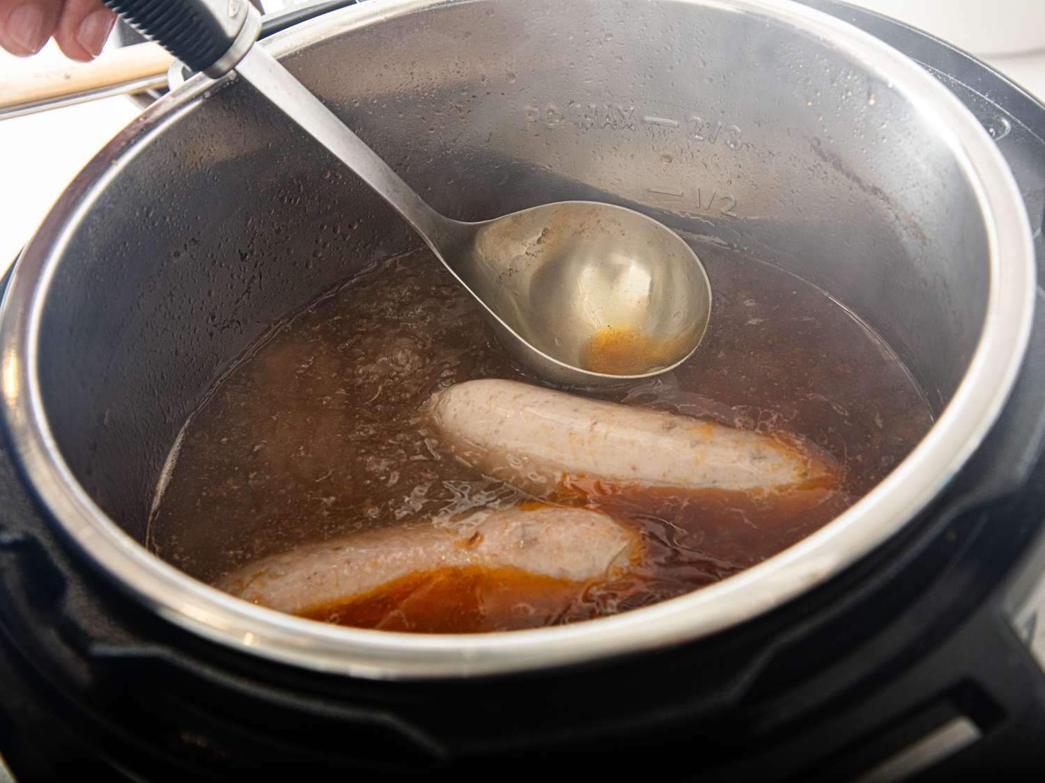 Cooking sausages in broth inside a pot with a ladle