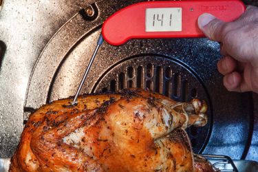 a person using an instant-read thermometer to take the temperature of a chicken roasting in the oven