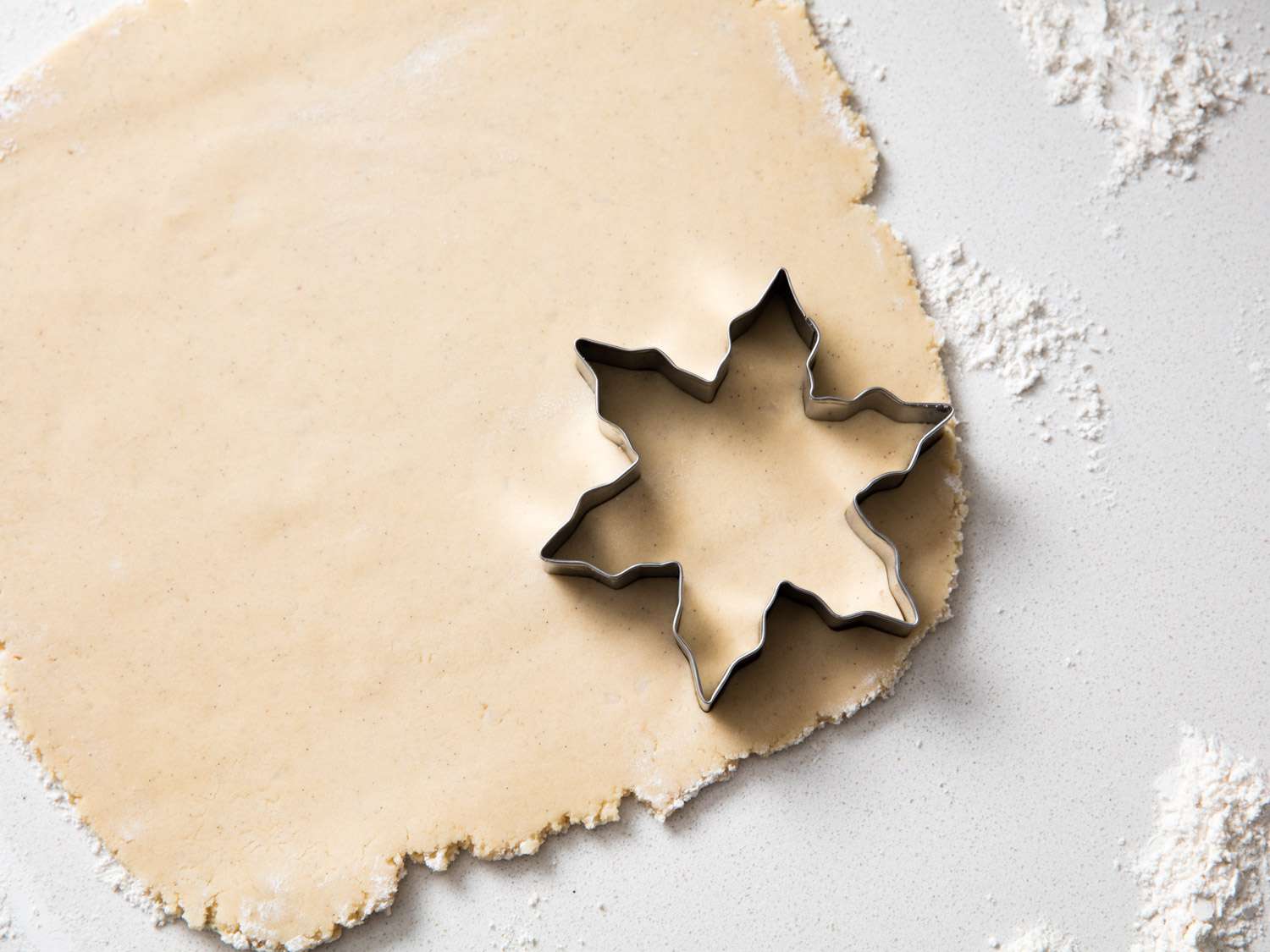 A starshaped cookie cutter on rolled dough sprinkled with flour on a surface