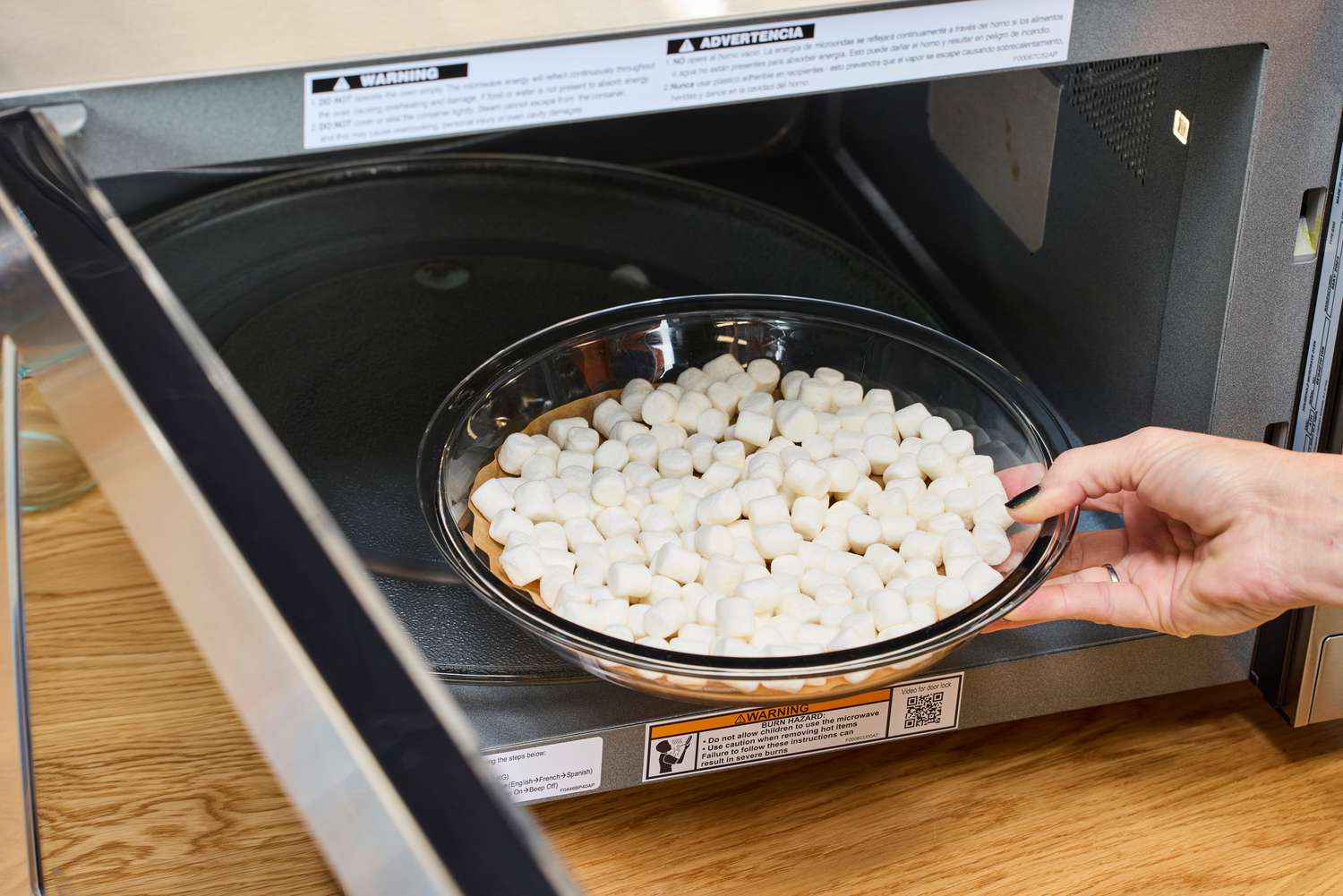 A person placing a filled bowl into the Panasonic - 2.2 Cu. Ft. 1250 Watt SD987SA Full-Size Microwave with Inverter