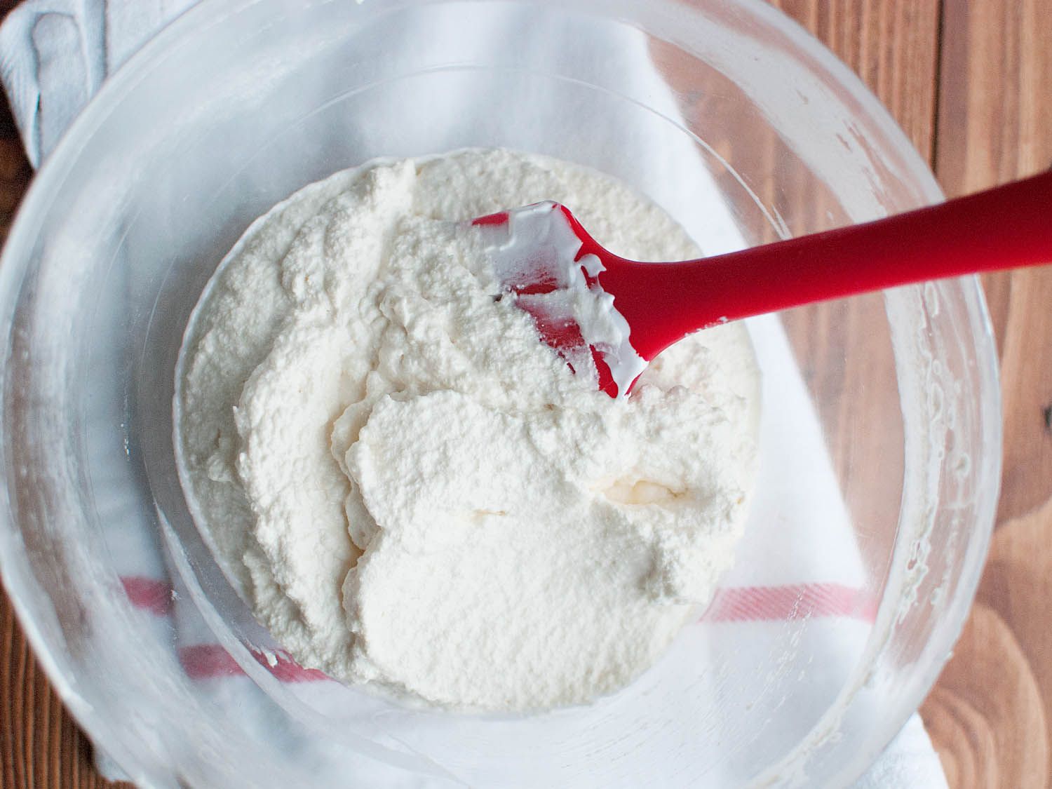 Buttercream mixture being stirred in a bowl with a spatula. 