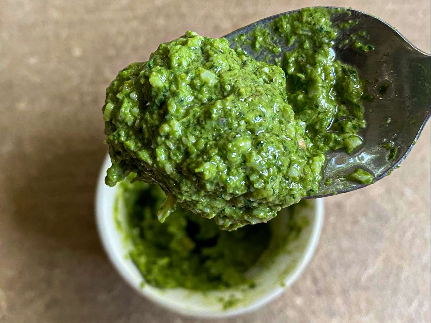 A spoonful of pesto with a container underneath