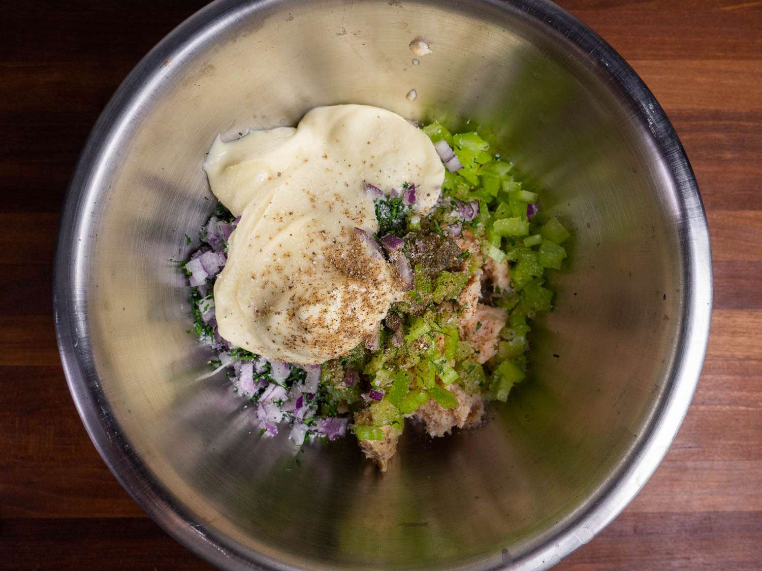 Tuna salad in a mixing bowl with lots of add-ins, including dill, celery, red onion, mayo, and more
