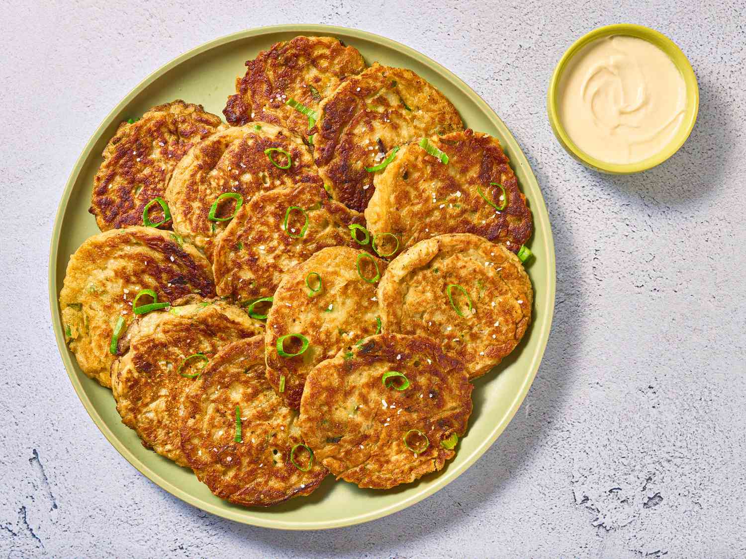 overhead of green platter boxty pancakes layed out with scallions and a side small bowl of sour cream