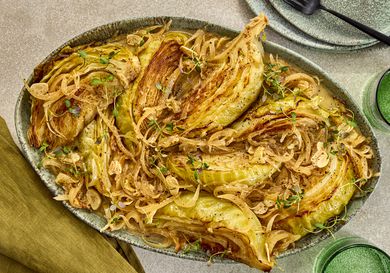cabbage on a platter with plates, forks and green napkins, and cups on the sides
