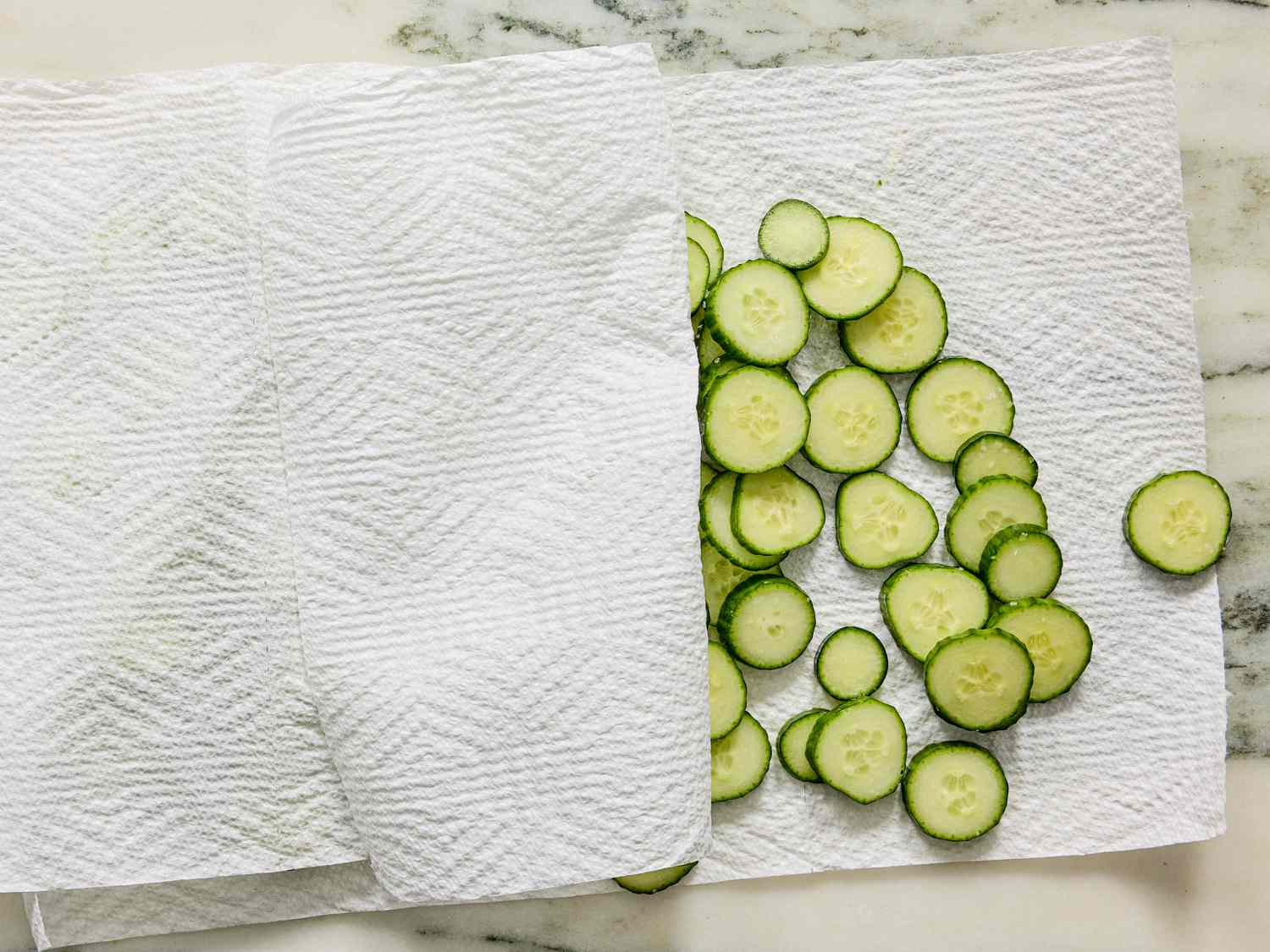 Cucumber slices on a paper towel on a marbled surface