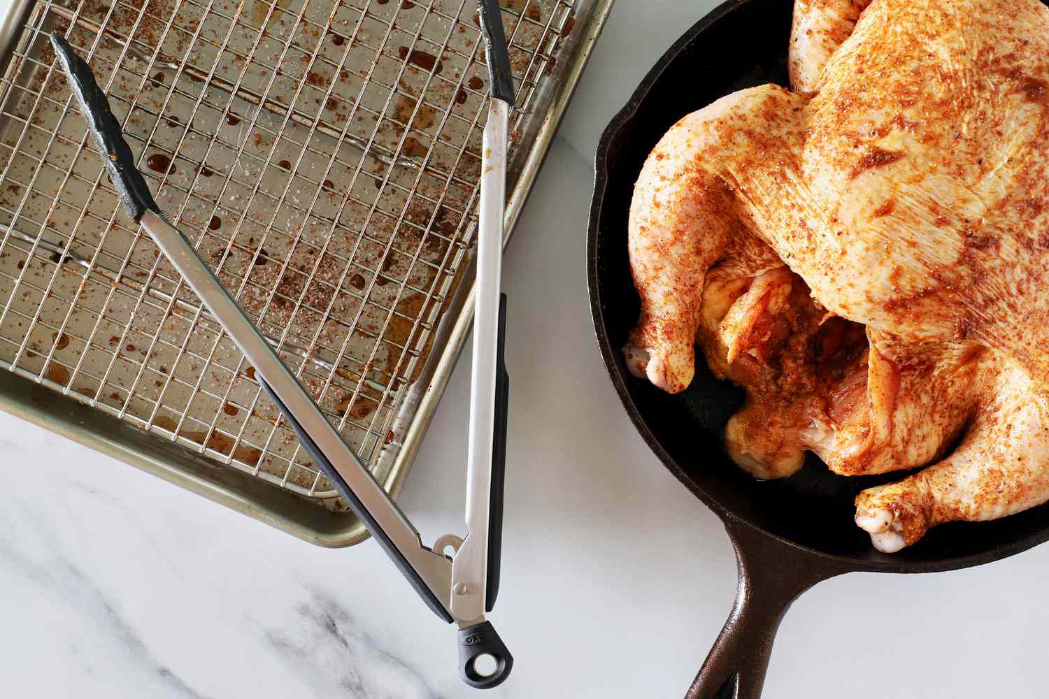 The OXO 12-Inch Silicone Tongs sitting on a baking sheet next to a chicken