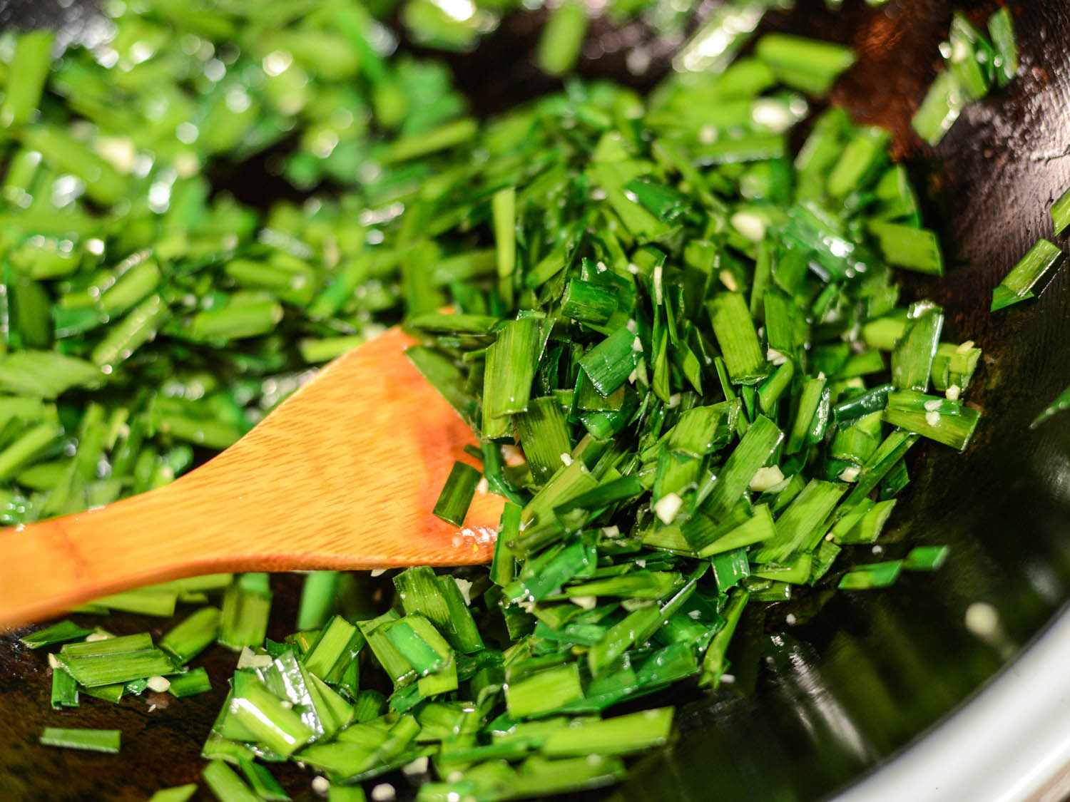 Tossing chopped Chinese chives in a skillet. 