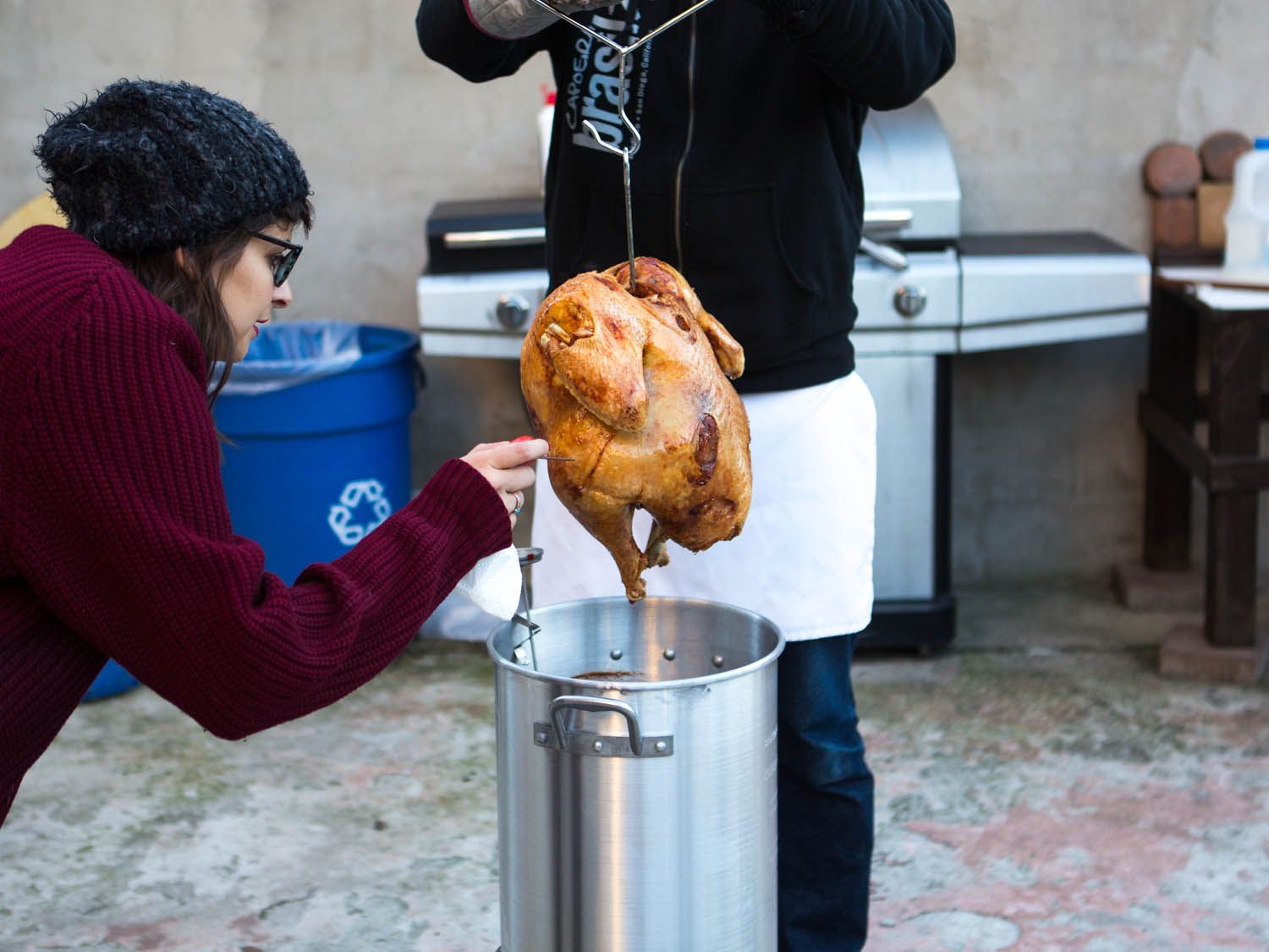 A person checking the temperature of a deep fried turkey that has been lifted out of pot of boiling oil.