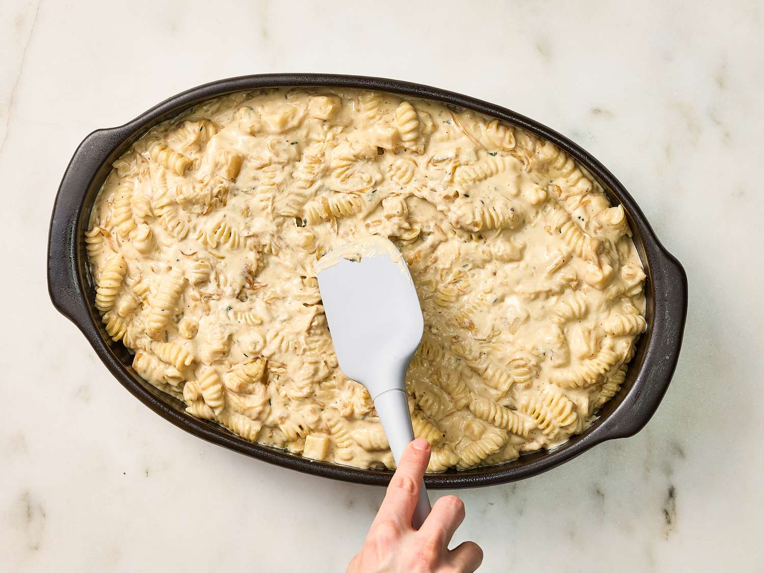 spreading pasta and cheese mixture into baking dish with spatula 