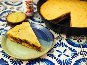 Tamale pie in a cast-iron skillet with a slice of it on a ceramic plate. 