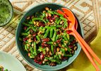 Bowl of mixed bean salad with greens and utensils on a patterned tablecloth