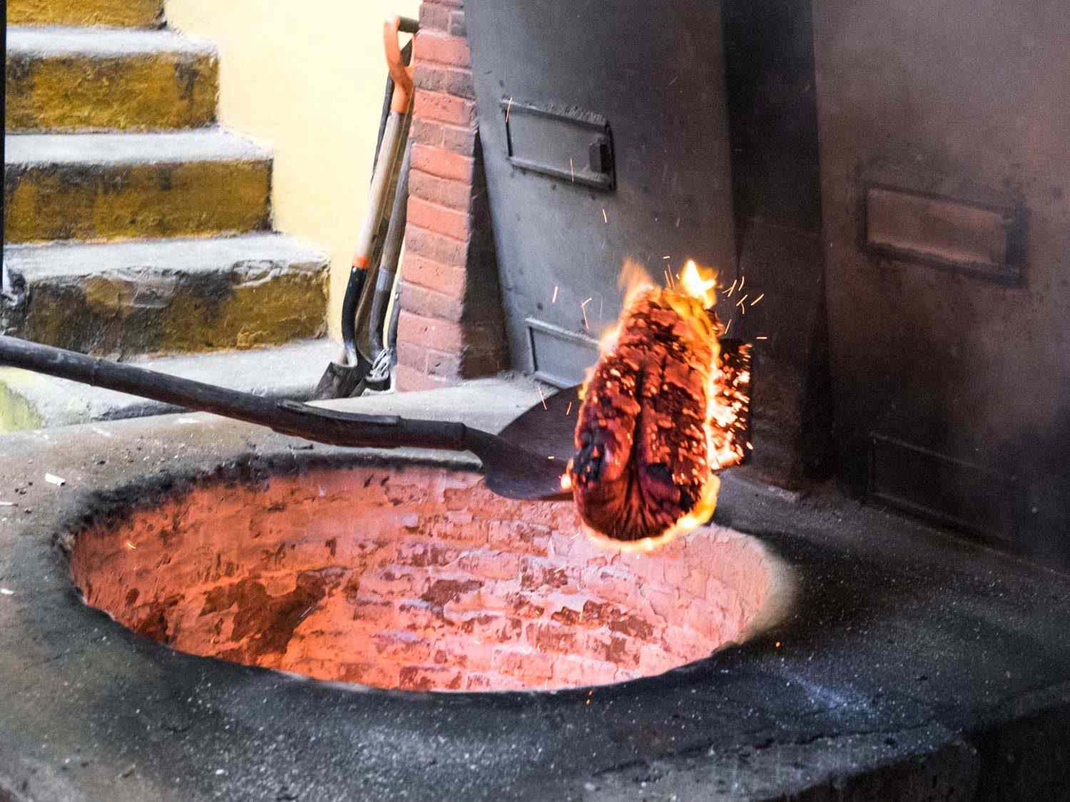 A glowing wood coal being pulled from an hoyo (pit oven) with a shovel.