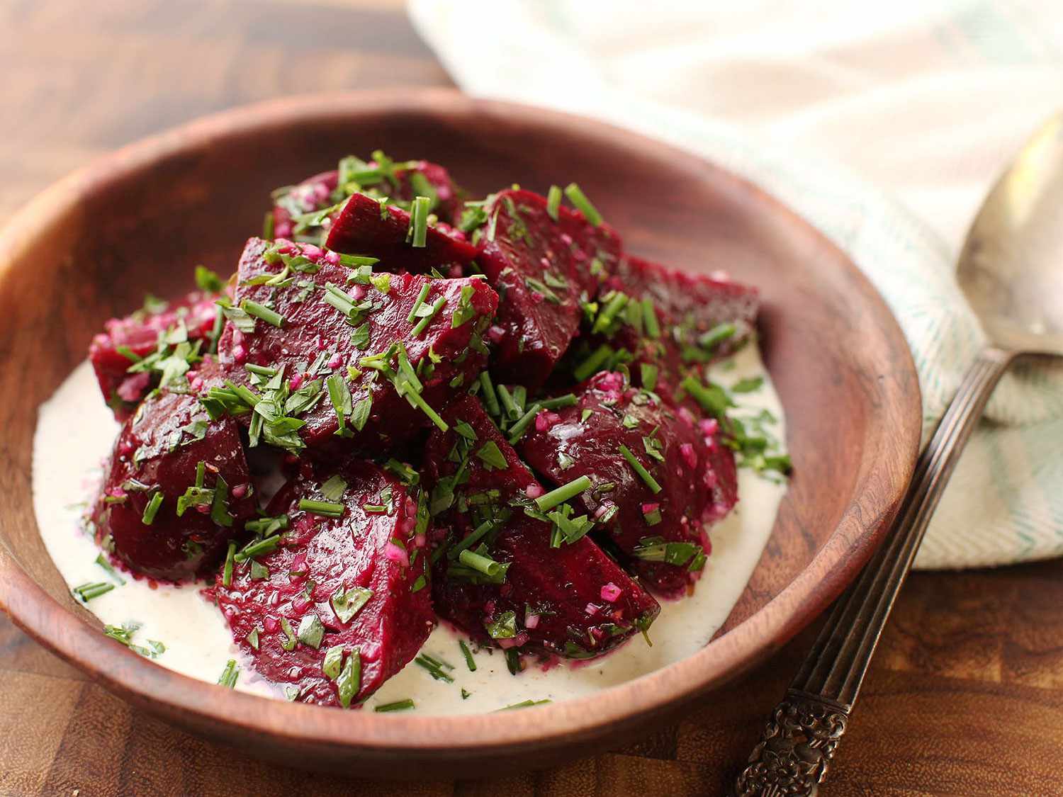 Roasted beets with on a pool of cream horseradish sauce sprinkled with chopped herbs and served up in a wooden bowl.