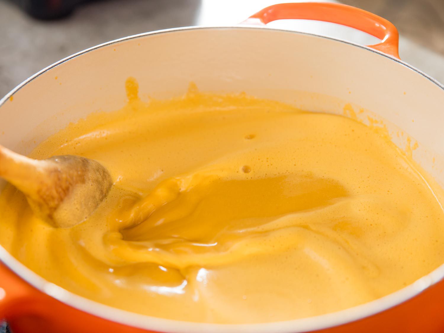 Light-orange lobster broth being stirred with a wooden spoon in a Dutch oven.