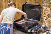 A person makes hamburgers using the Weber Slate 22 inch Rust-Resistant Tabletop Griddle