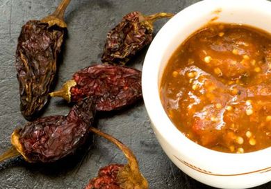 A small bowl of chile morita salsa next to some dried morita chiles. 