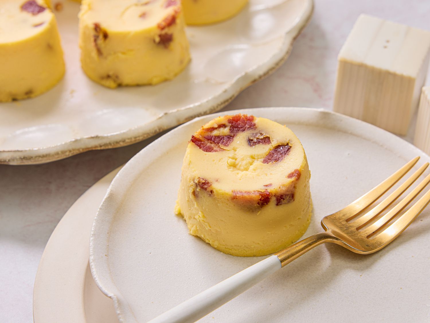 Egg bite on a small plate, with a platter of more bites and a pepper shaker on the side