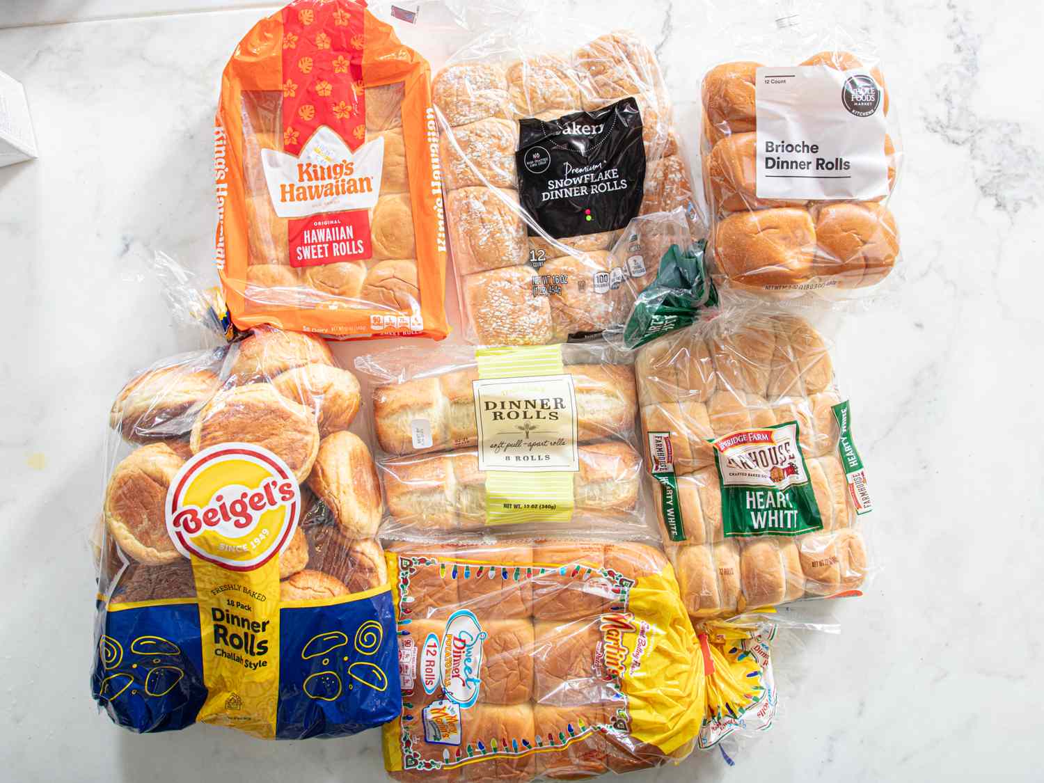 Various brands of packaged dinner rolls placed on a table including Kings Hawaiian and others