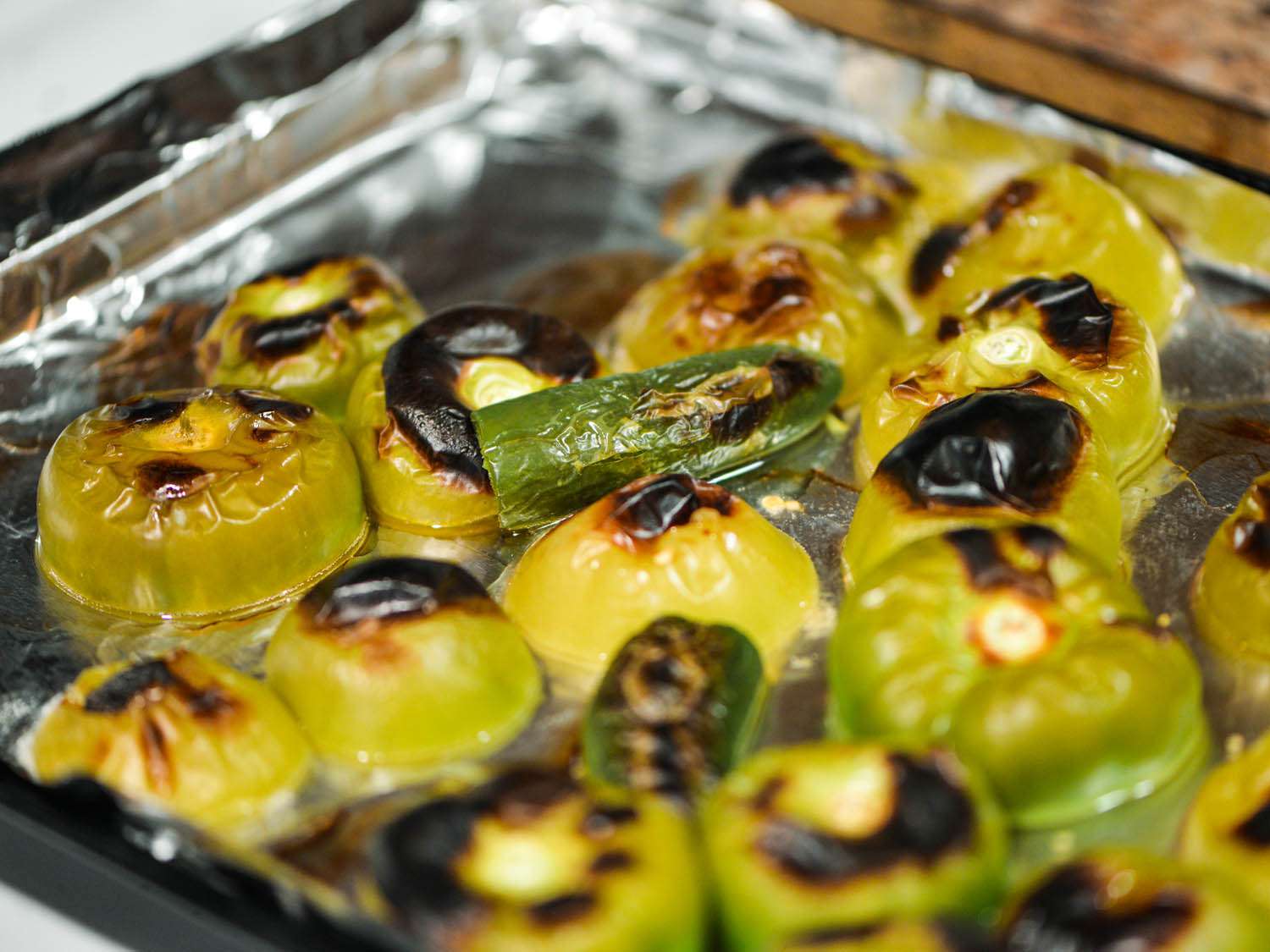 Roasted charred green chiles and tomatillos on foil-lined pan